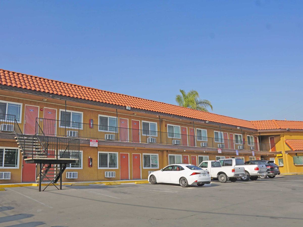 A two-story motel with a parking lot in front, featuring several parked cars and exterior staircases.