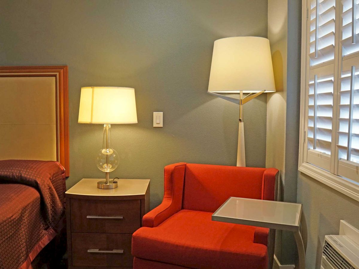 The image shows a cozy bedroom corner with two lamps, an orange armchair, a nightstand, and window shutters on the right wall, ending the sentence.