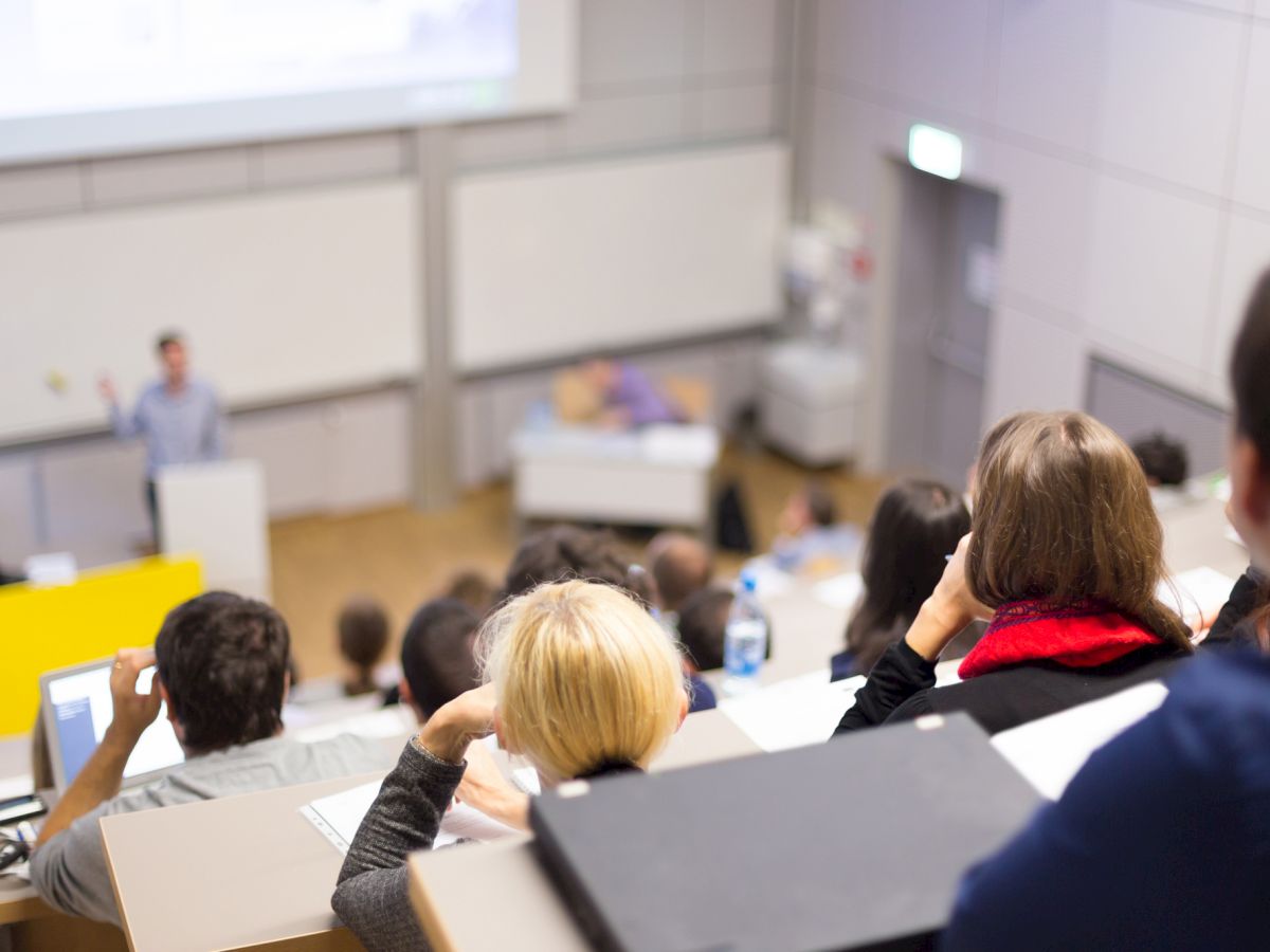 A group of people is attending a lecture in a modern classroom, focusing on a speaker presenting information in the front.