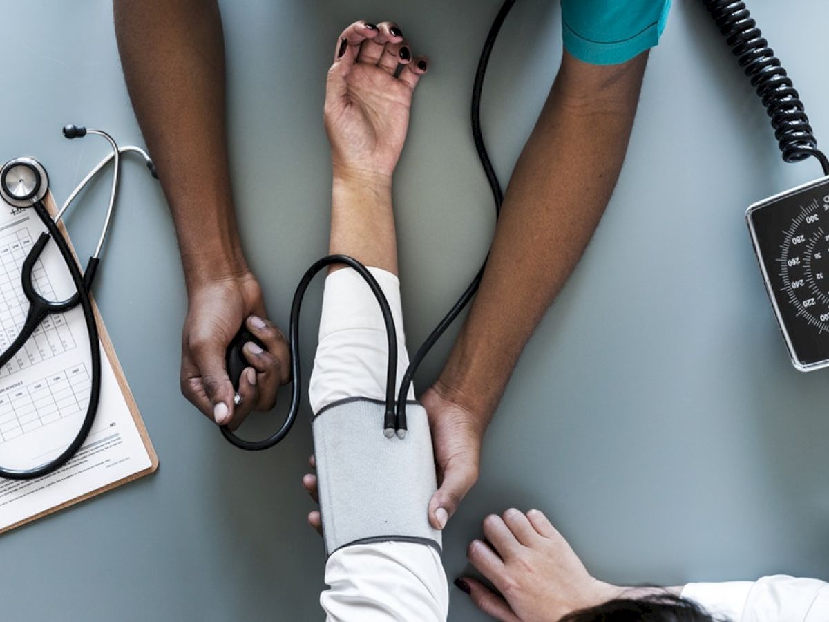 A healthcare professional is measuring a patient's blood pressure using a sphygmomanometer. There is also a clipboard with a chart and a stethoscope.